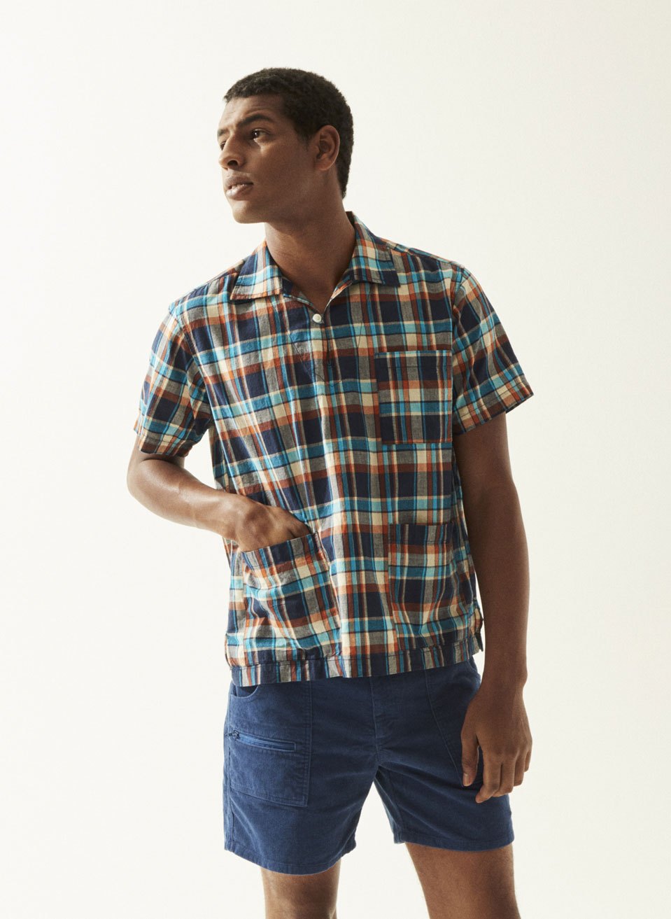 Man wearing a blue, orange and white plaid short-sleeve shirt and navy shorts by Battenwear.