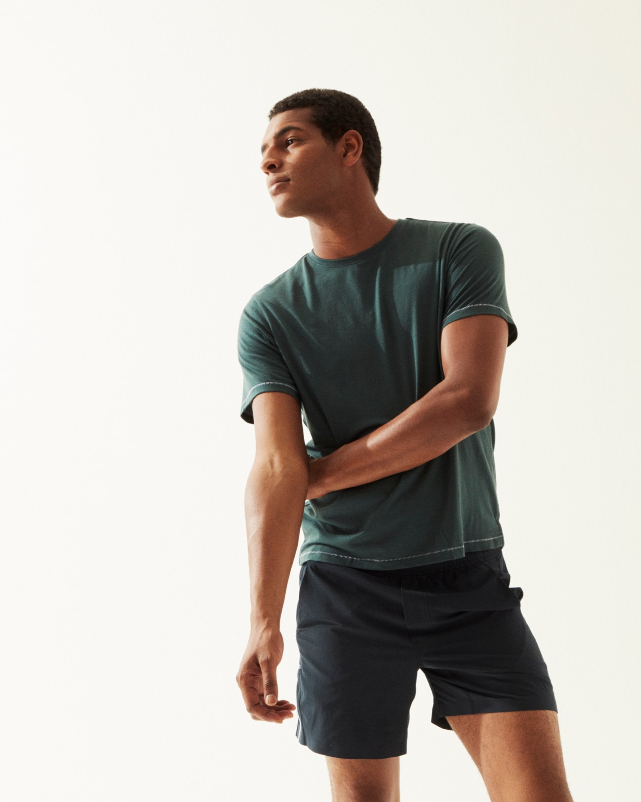 Man wearing a dark green t-shirt and navy shorts by Torsa against a white background.
