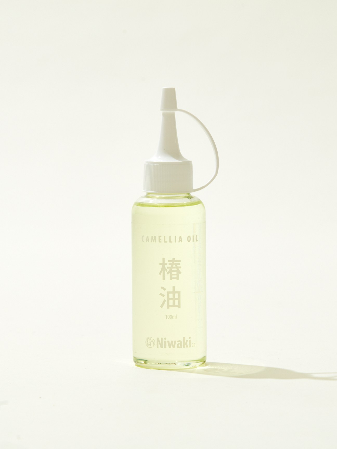 Bottle of Niwaki camellia oil with white cap and clear bottle containing light green oil