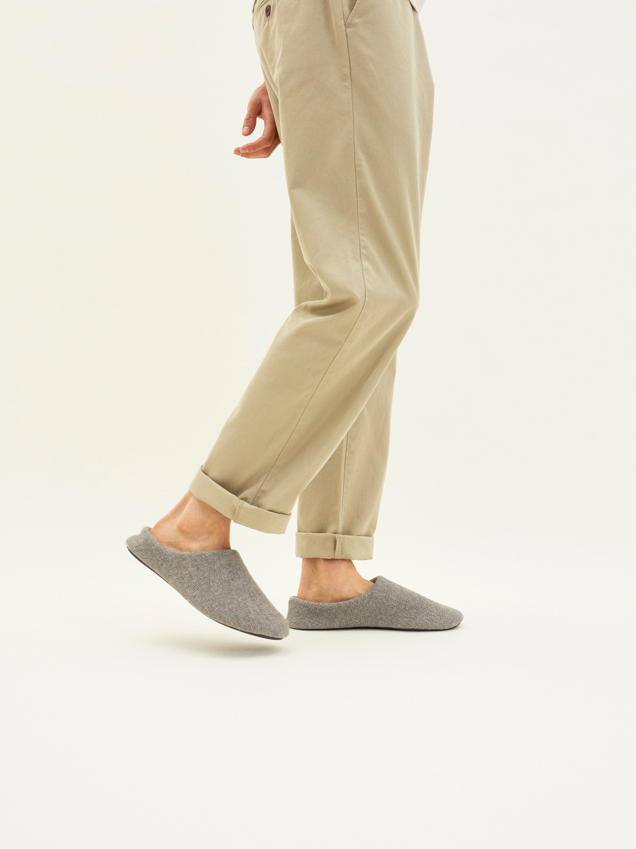 Person wearing beige rolled-up trousers and grey textured cotton slippers against neutral background