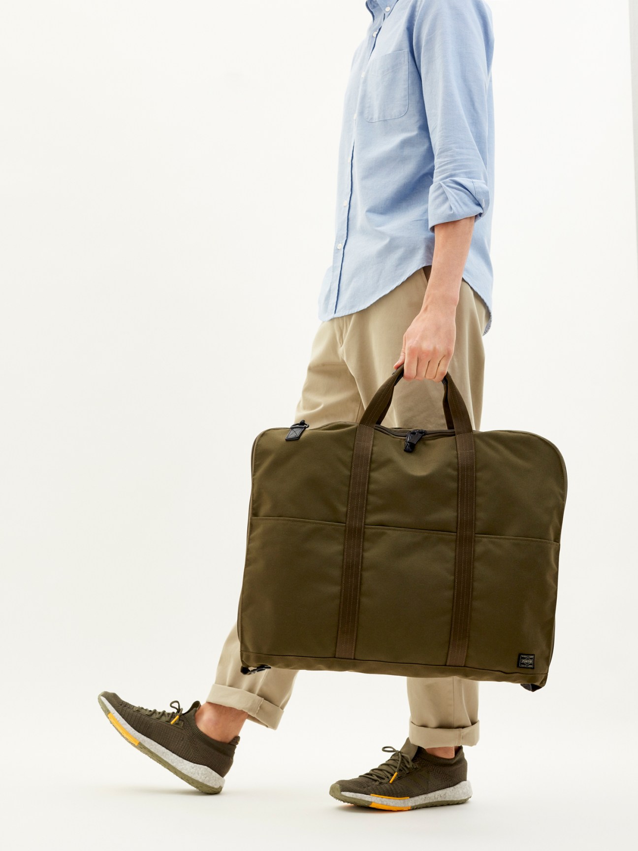 Person carrying olive green Porter x Monocle suit bag while walking