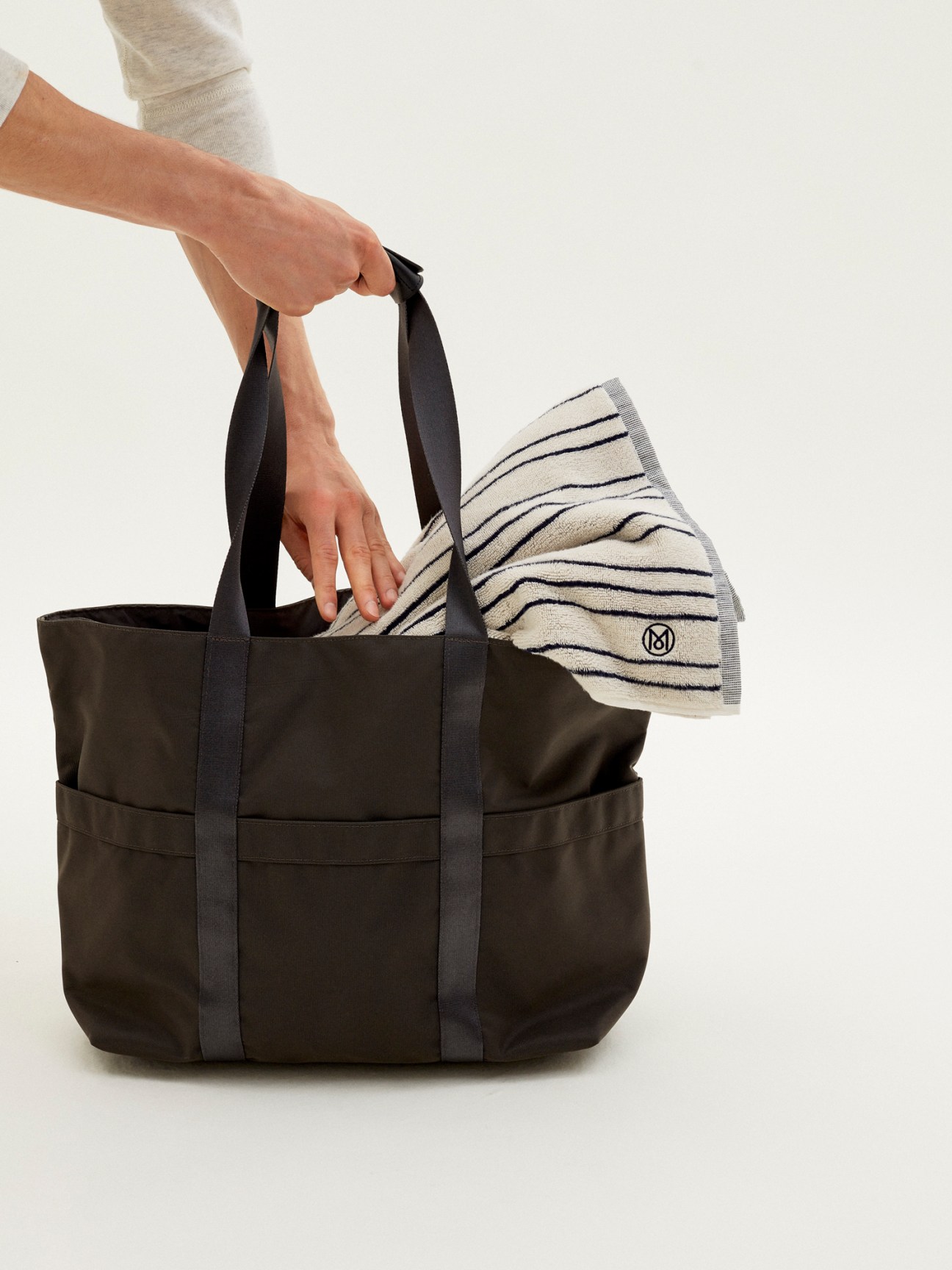 Dark grey tote bag being carried by hand with striped towel visible inside
