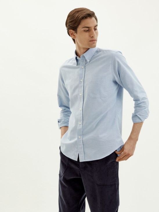 Man wearing light blue button-down classic shirt by Trunk x Monocle with dark trousers.