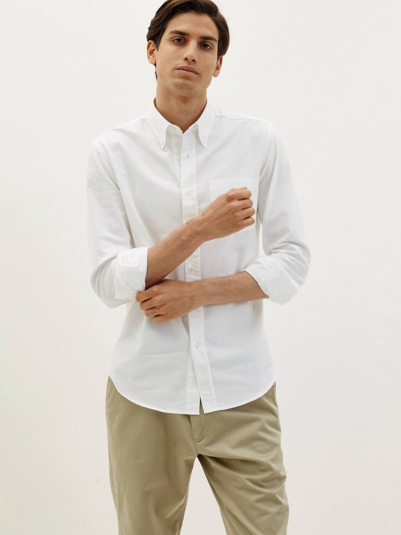 Man wearing white Trunk x Monocle button-down classic shirt with beige trousers against neutral background