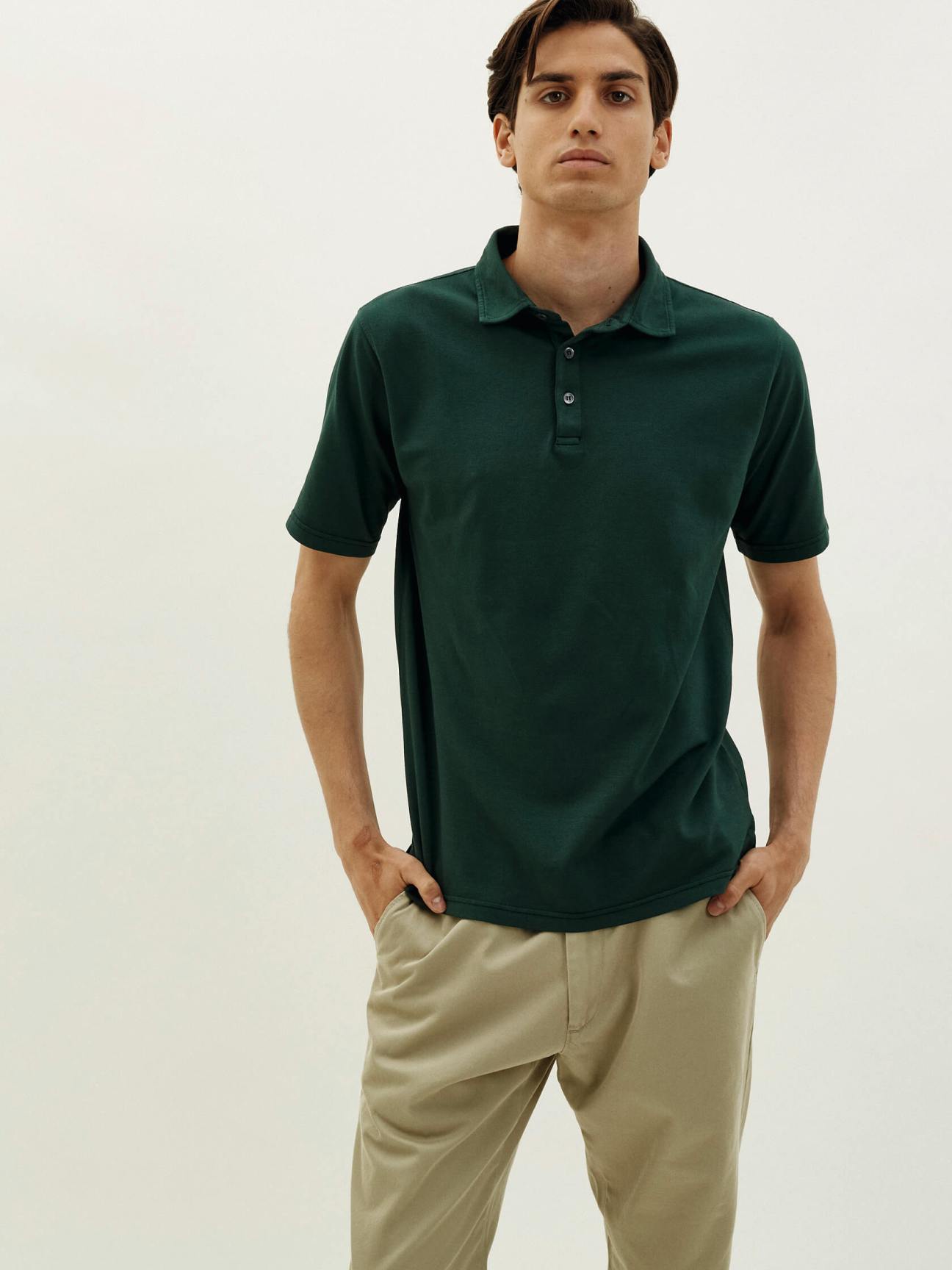 Man wearing forest green polo shirt with beige chinos against neutral background
