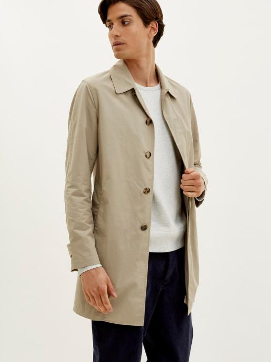 Man wearing beige unlined mac by Valstar x Monocle over white shirt and navy trousers.