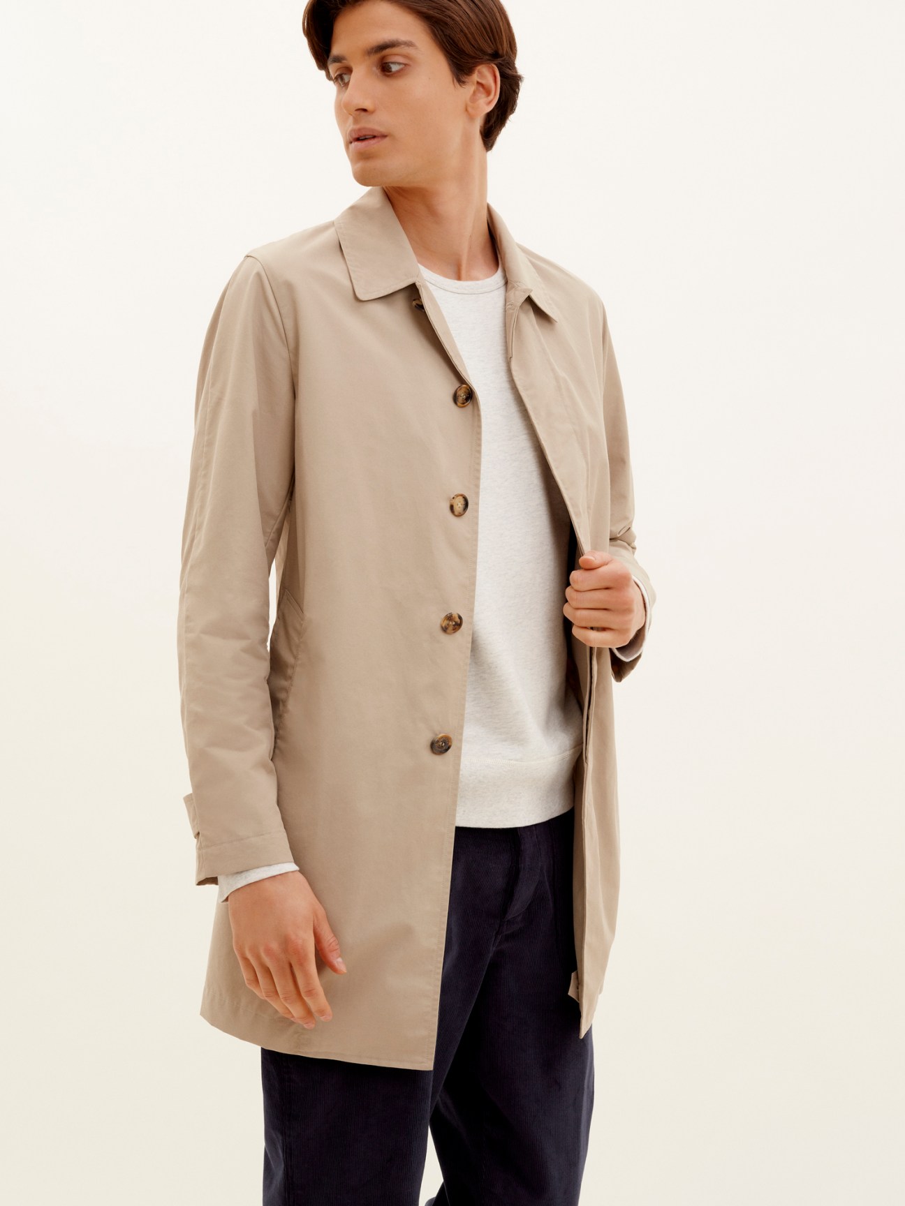 Man wearing beige Valstar x Monocle unlined mac trench coat over white t-shirt and dark trousers