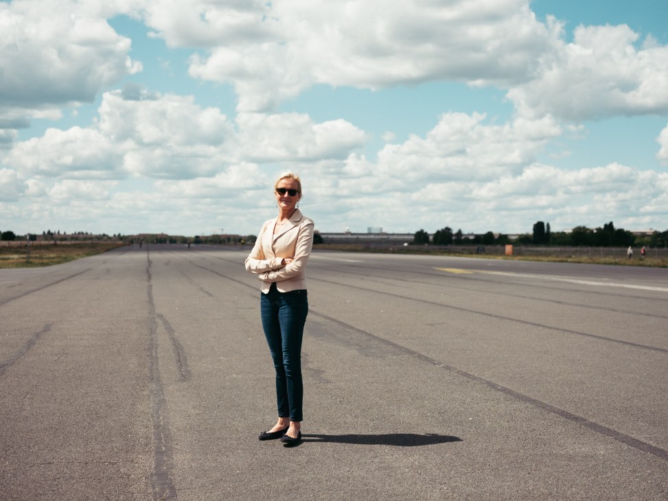 Benita von Maltzahn standing on an airport runway wearing sunglasses, white blazer and jeans