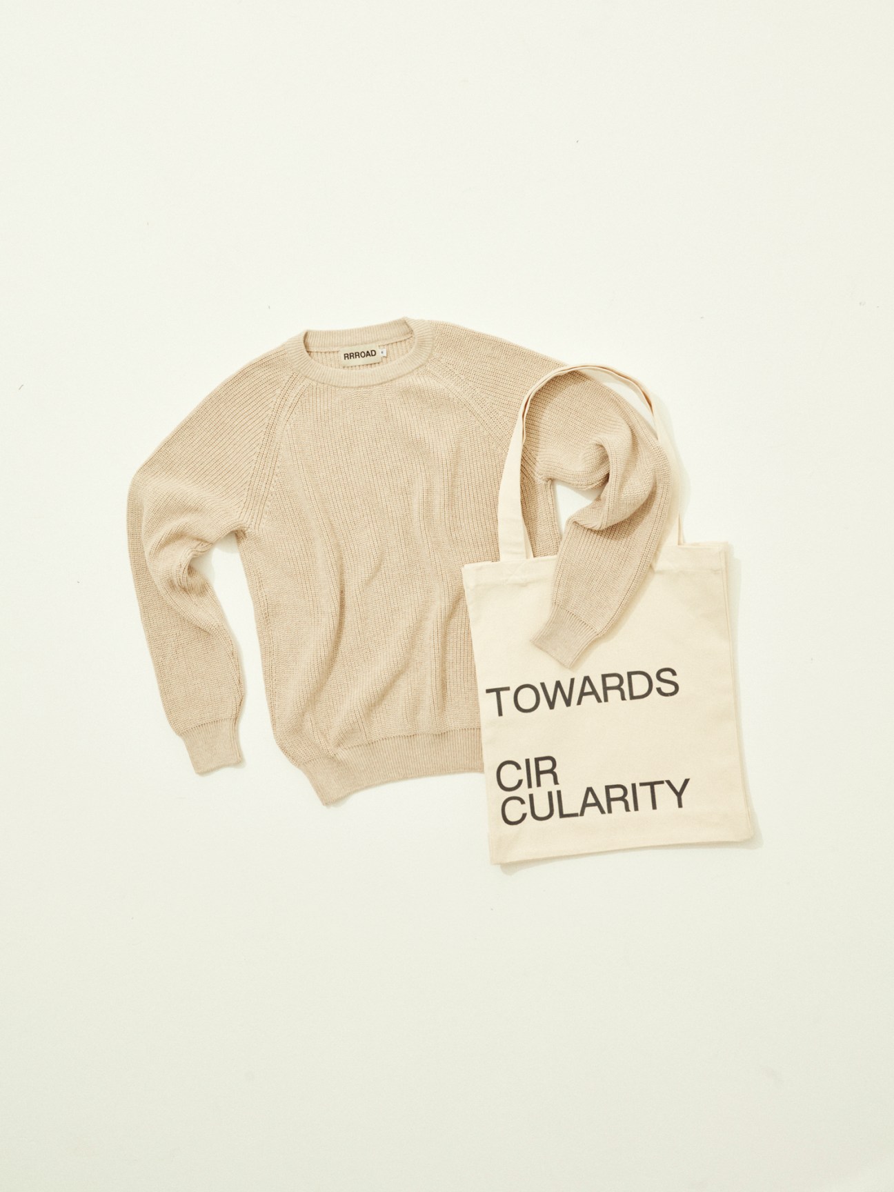 RRRoad cream knit sweater and canvas tote bag with 'TOWARDS CIRCULARITY' text on neutral background