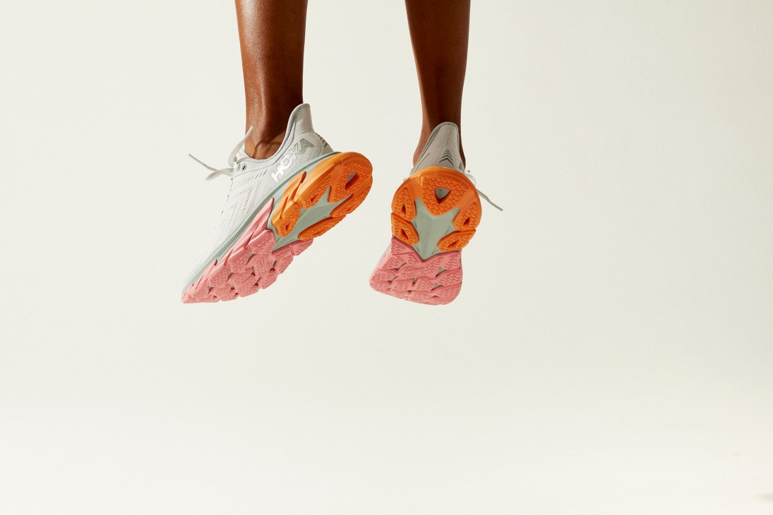 Clifton Edge by Hoka One One running shoes in mid-air showing distinctive pink and orange sole cushioning