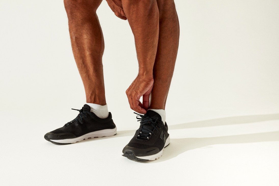 Person in black Boulder trainers by Active 88 with white Adidas socks touching ankle