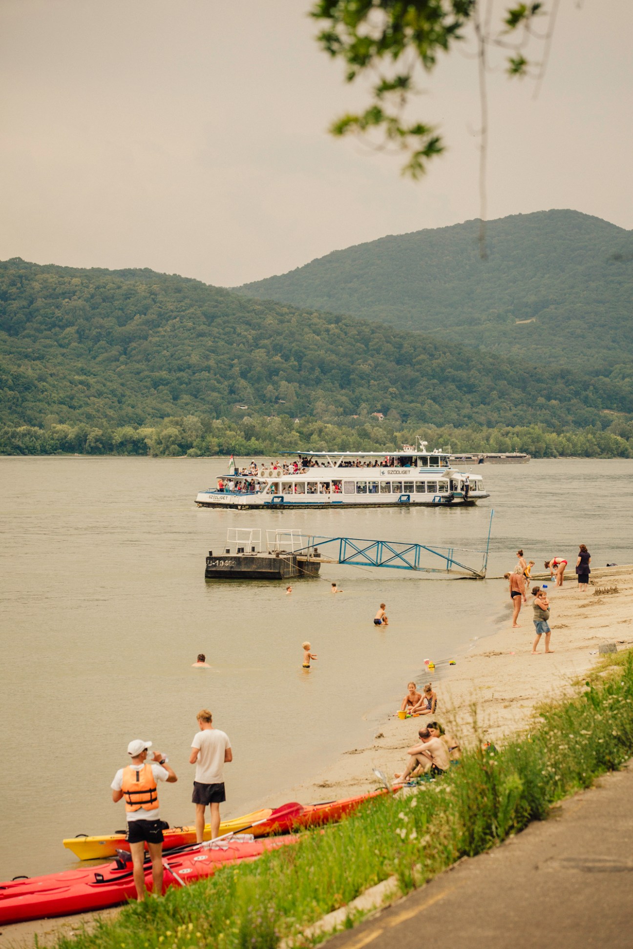 Ferry boat on the Danube with passengers, swimming area and forested hills in background
