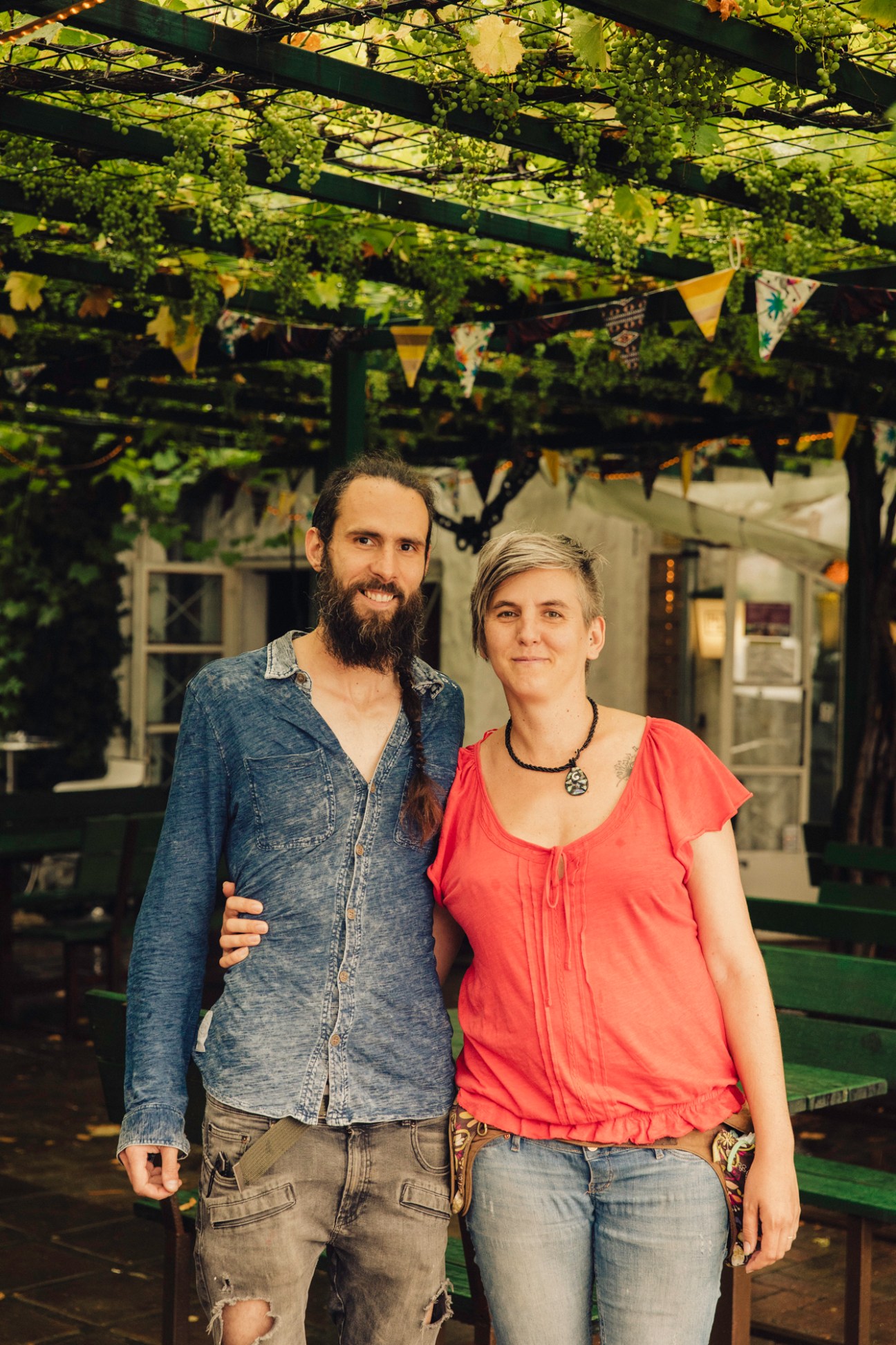 Couple standing under grape vine pergola with decorative bunting at outdoor dining area