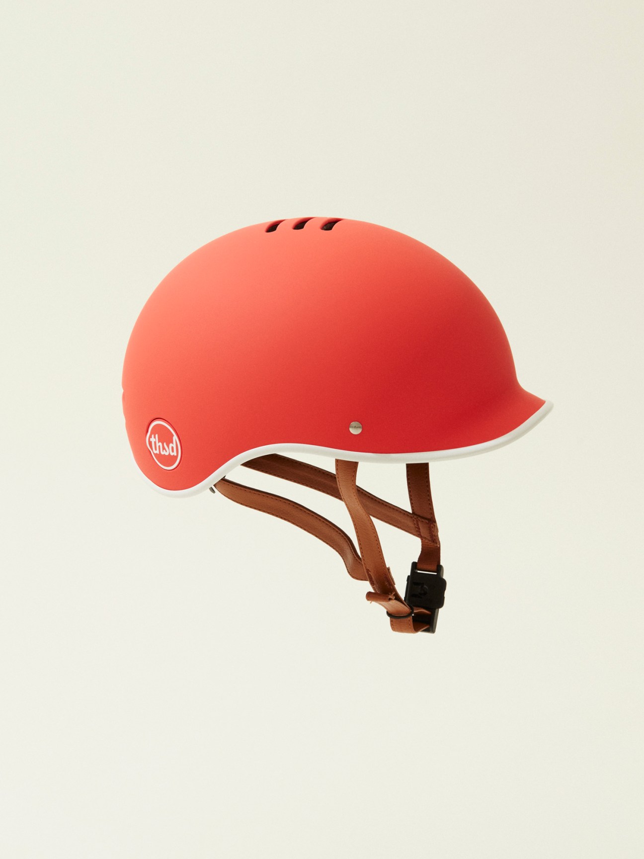 Red bike helmet with ventilation holes and brown leather straps on white background