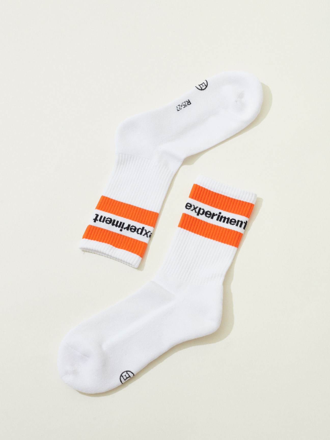 Pair of white athletic socks with orange stripes and experiment text on white background