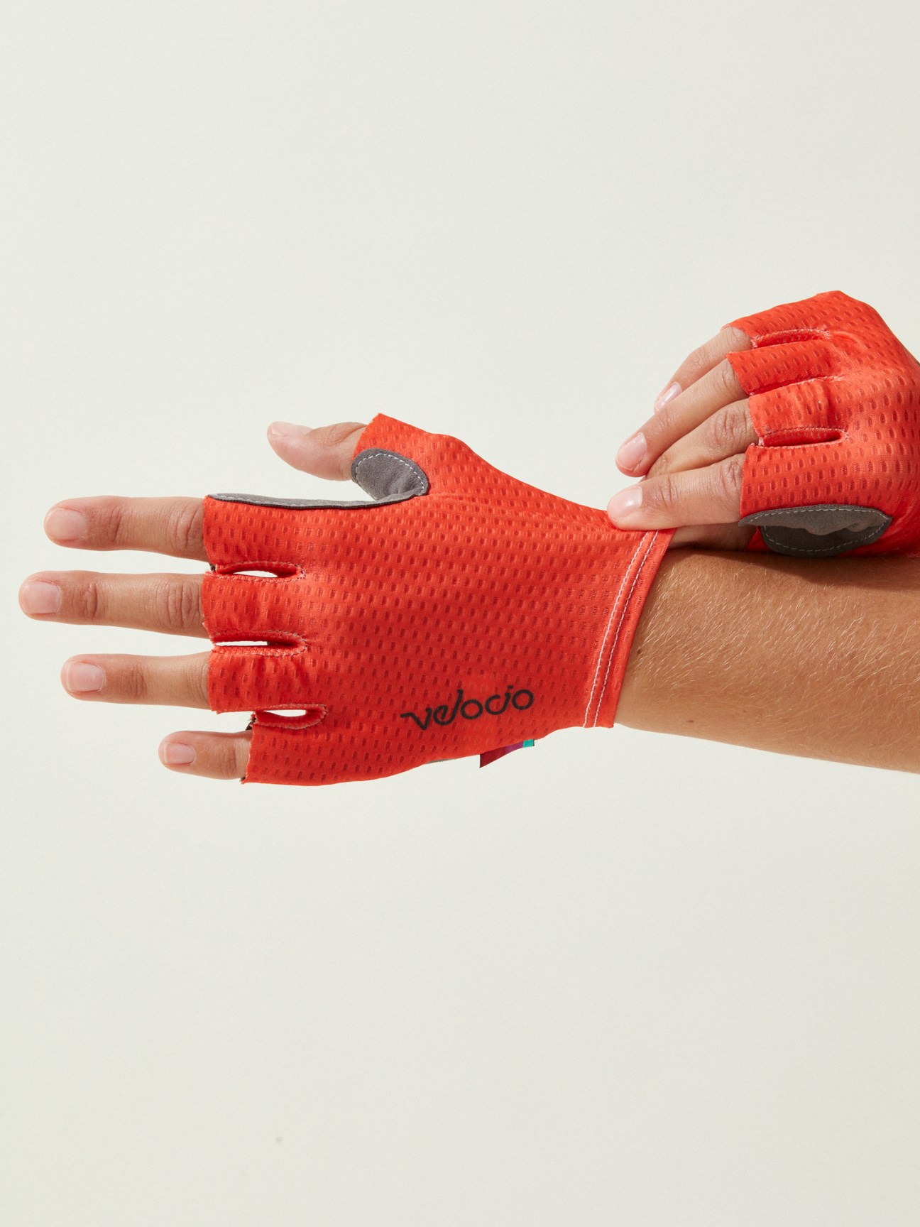 Red Velocio cycling gloves with perforated palms and gray padding worn on hands against white background