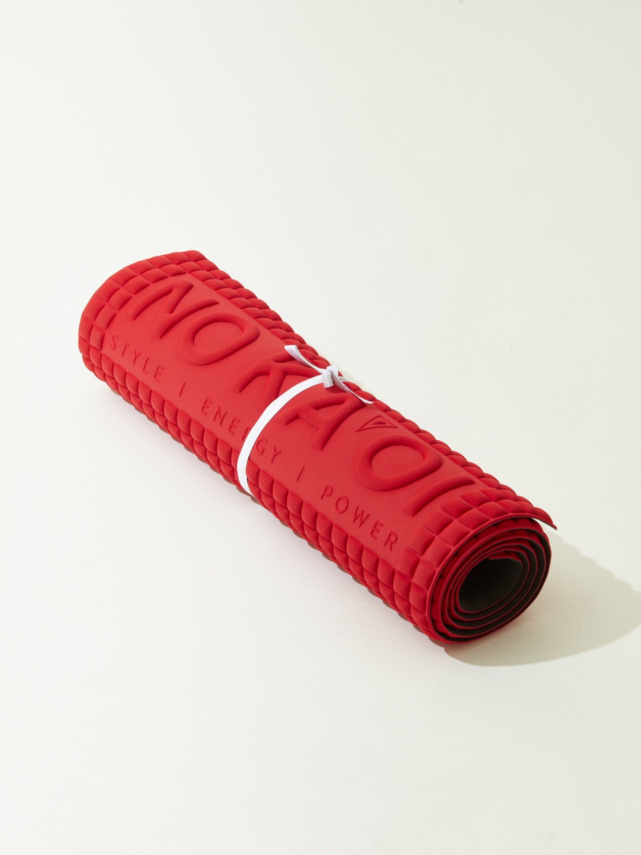 Red yoga mat with textured surface and white logo rolled up on white background