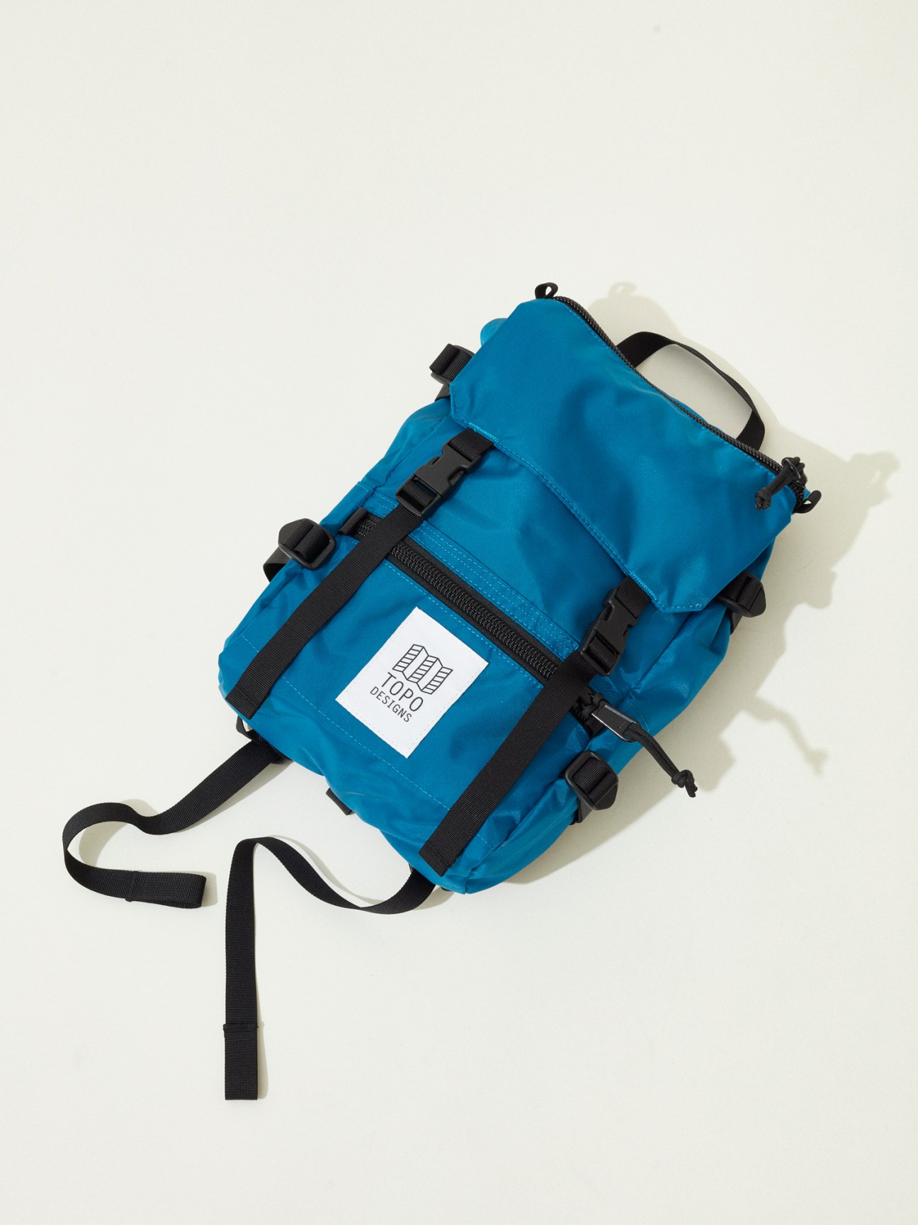 Blue Topo Designs backpack with black straps and white label on white background