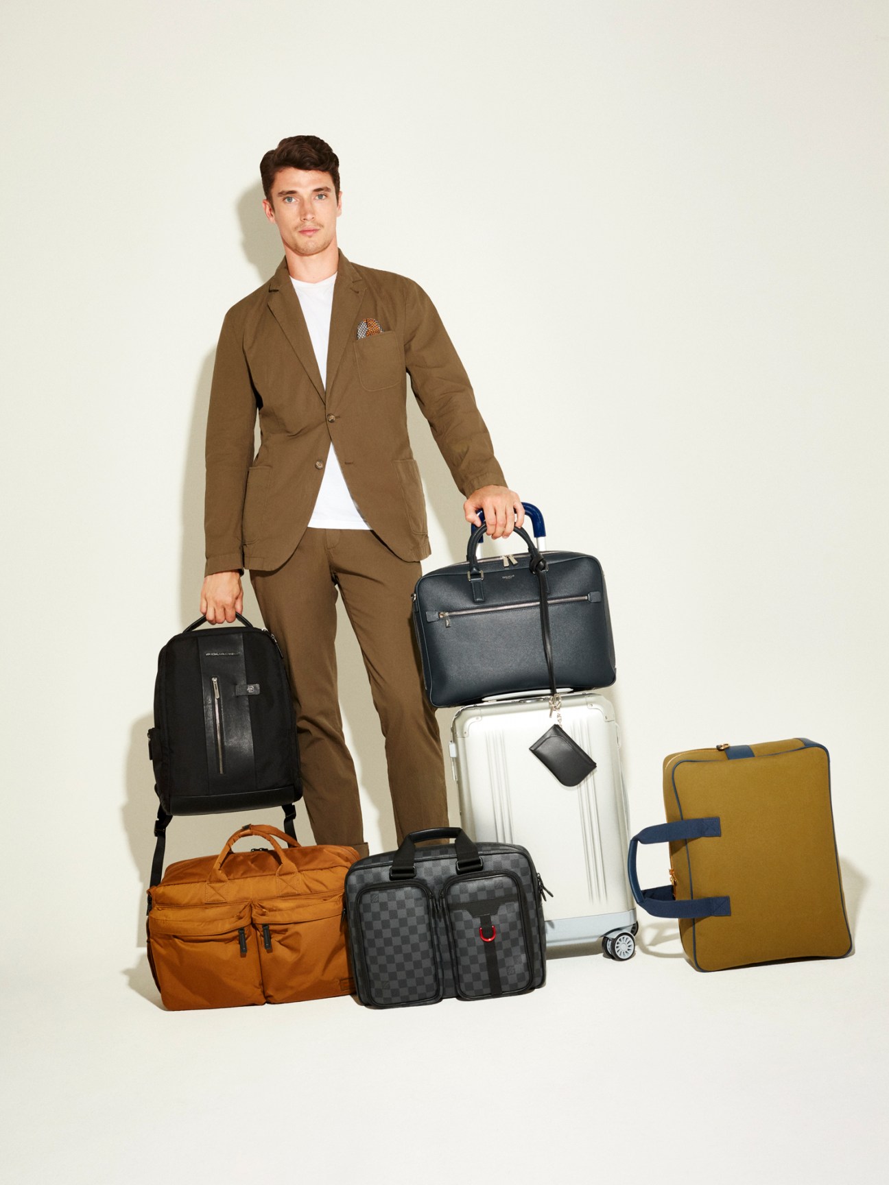 Man in brown suit holding multiple bags and suitcases for business travel.