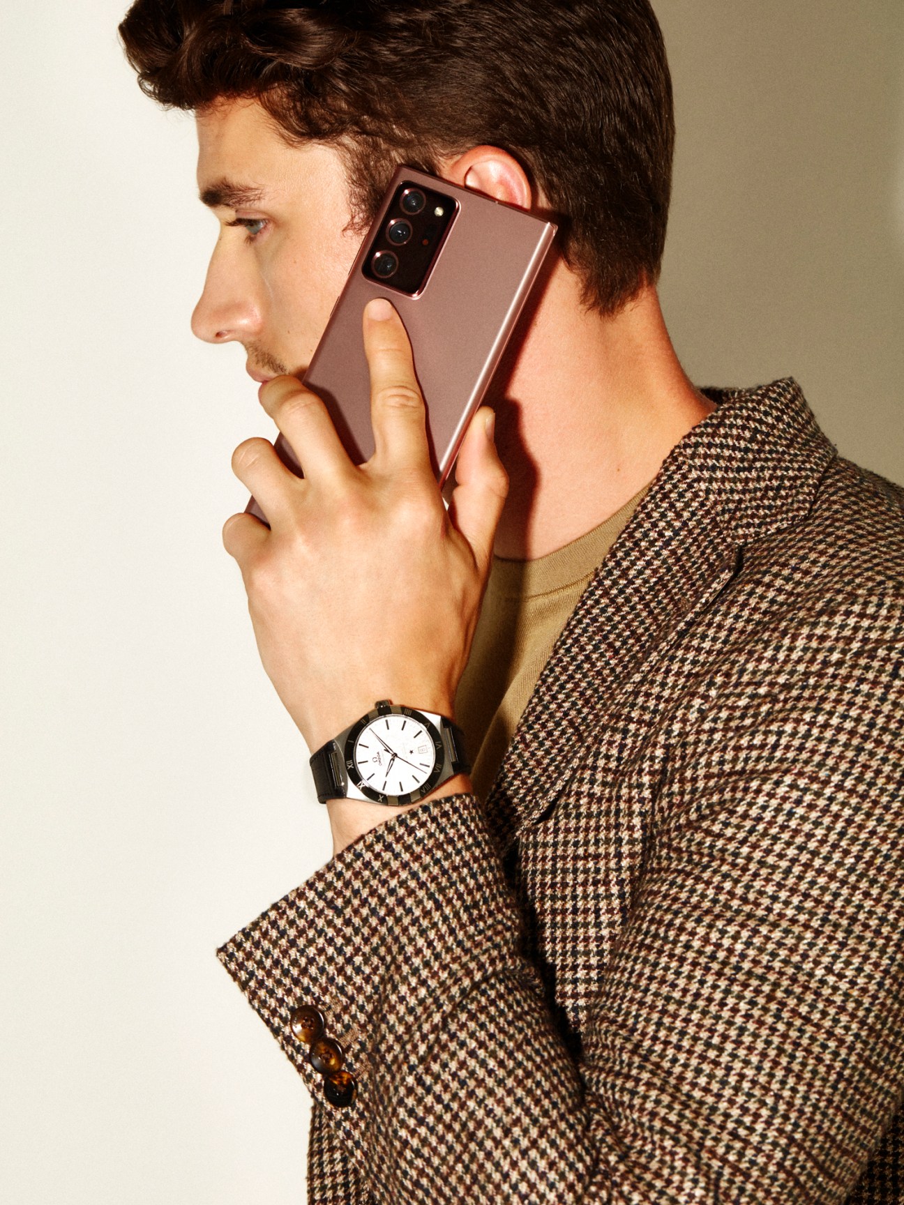 Man in profile holding a rose-gold Samsung Galaxy Note 20 5G phone, wearing a Boglioli jacket and Salvatore Ferragamo t-shirt with an Omega Constellation watch.