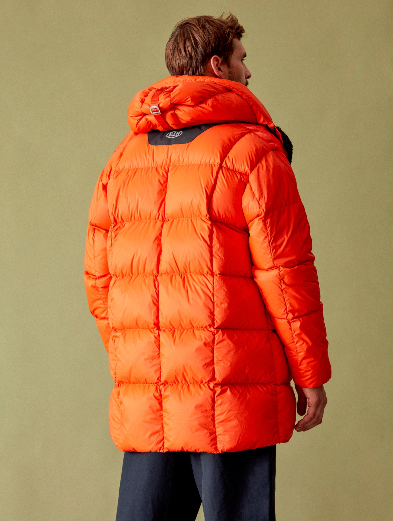 Model wearing bright orange quilted down coat with hood over dark trousers