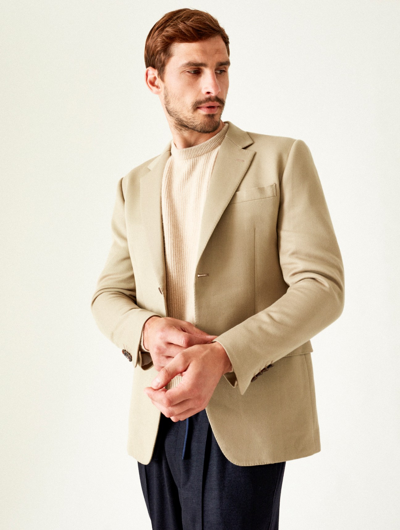 Model wearing beige blazer over cream ribbed turtleneck sweater with dark trousers