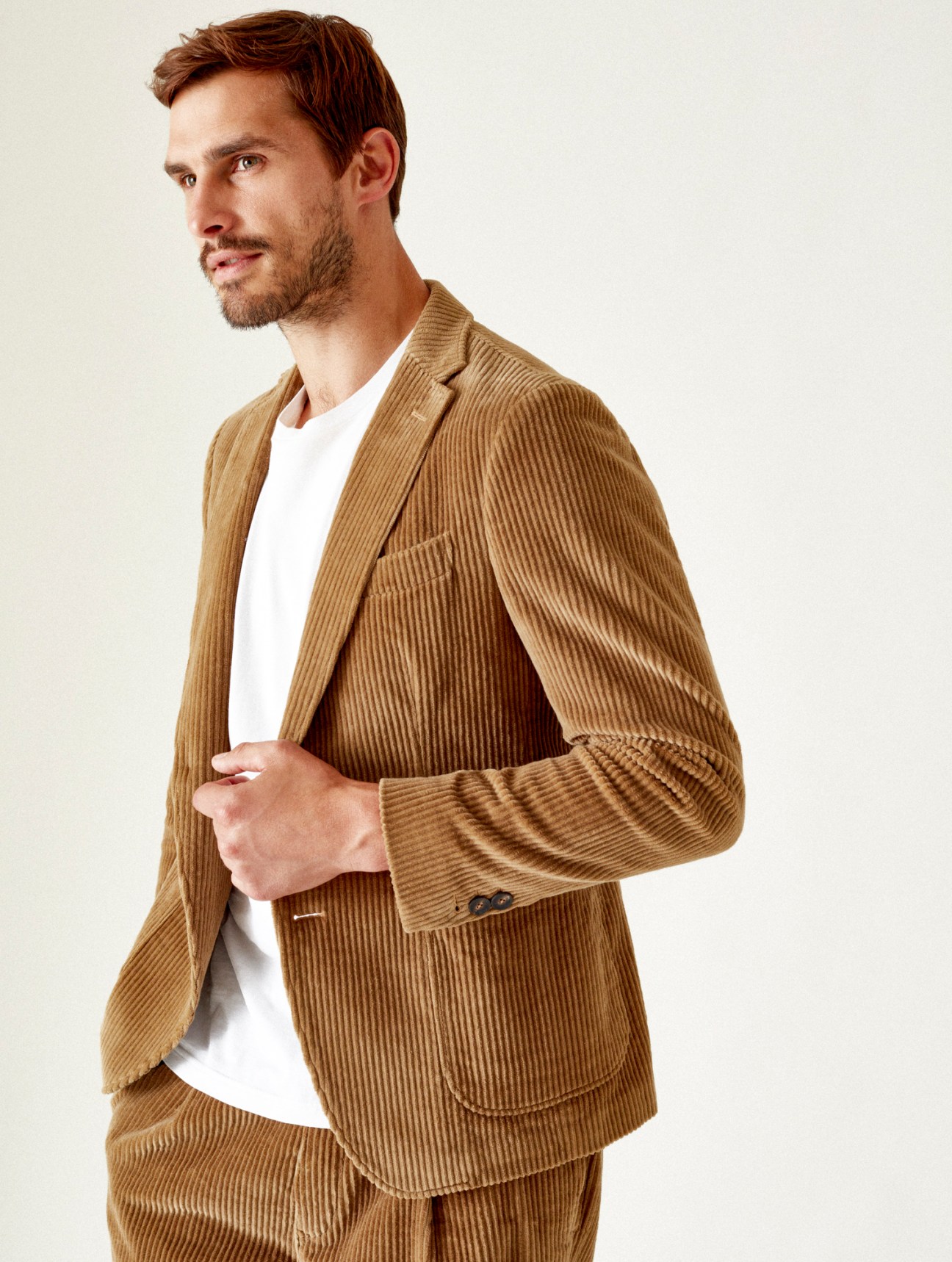 Model wearing tailored tan corduroy jacket and matching trousers with white t-shirt underneath