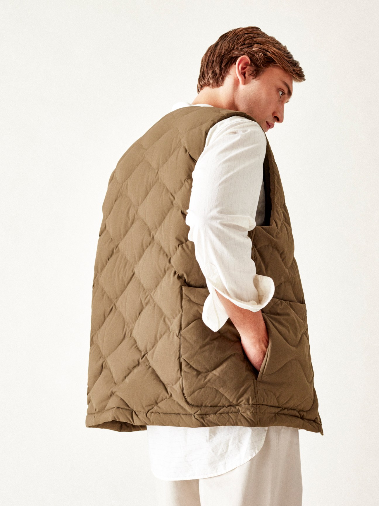 Model wearing olive quilted gilet over white shirt and beige trousers