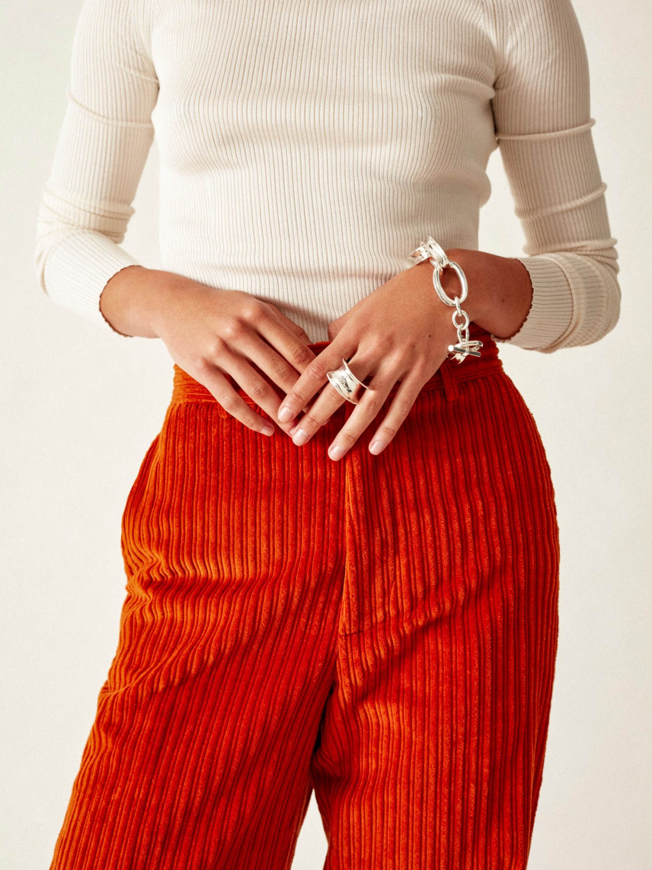 Model wearing cream ribbed rollneck jumper and rust red corduroy trousers with silver bracelet and ring