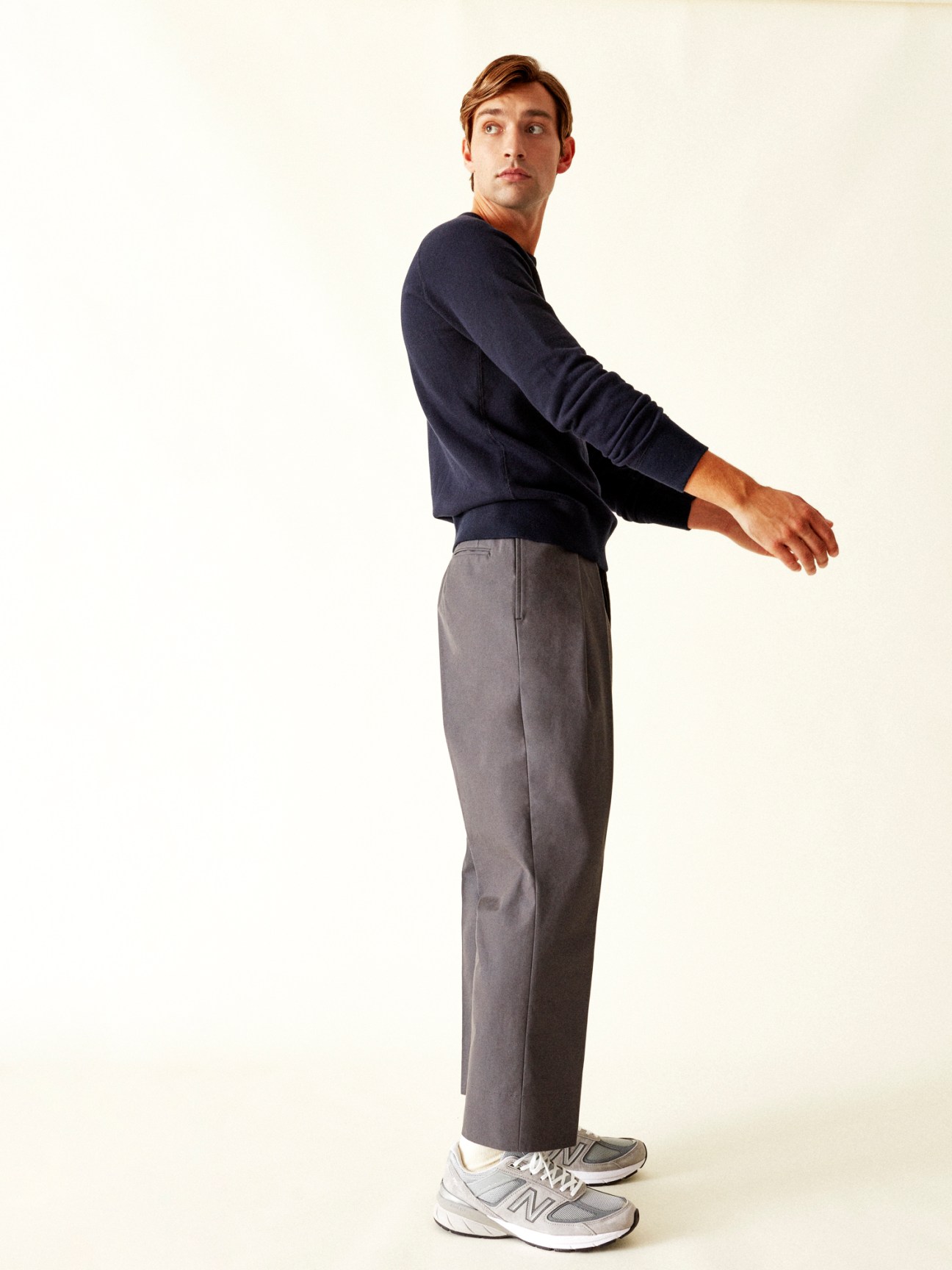 Model wearing navy sweatshirt and grey trousers with grey sneakers against light background