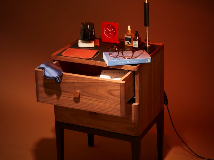 Mid-century walnut bedside table with open drawer, lamp, clock, glasses, books and small bottles on top