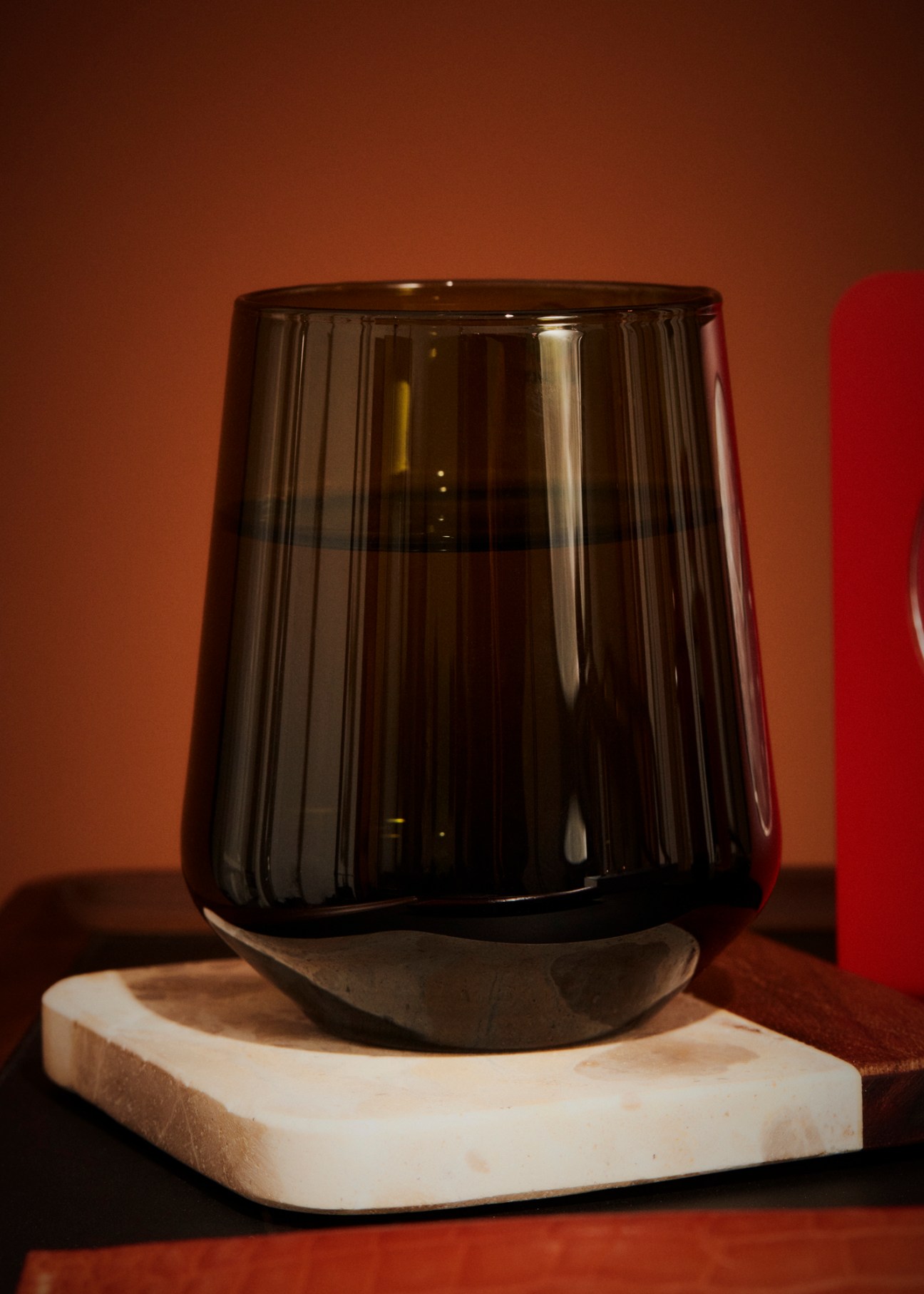 Clear glass tumbler with ribbed texture sitting on marble coaster against warm background