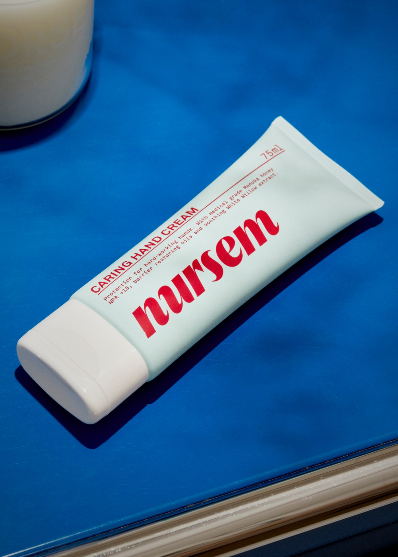 Nursem hand cream tube with white packaging and red branding on blue surface