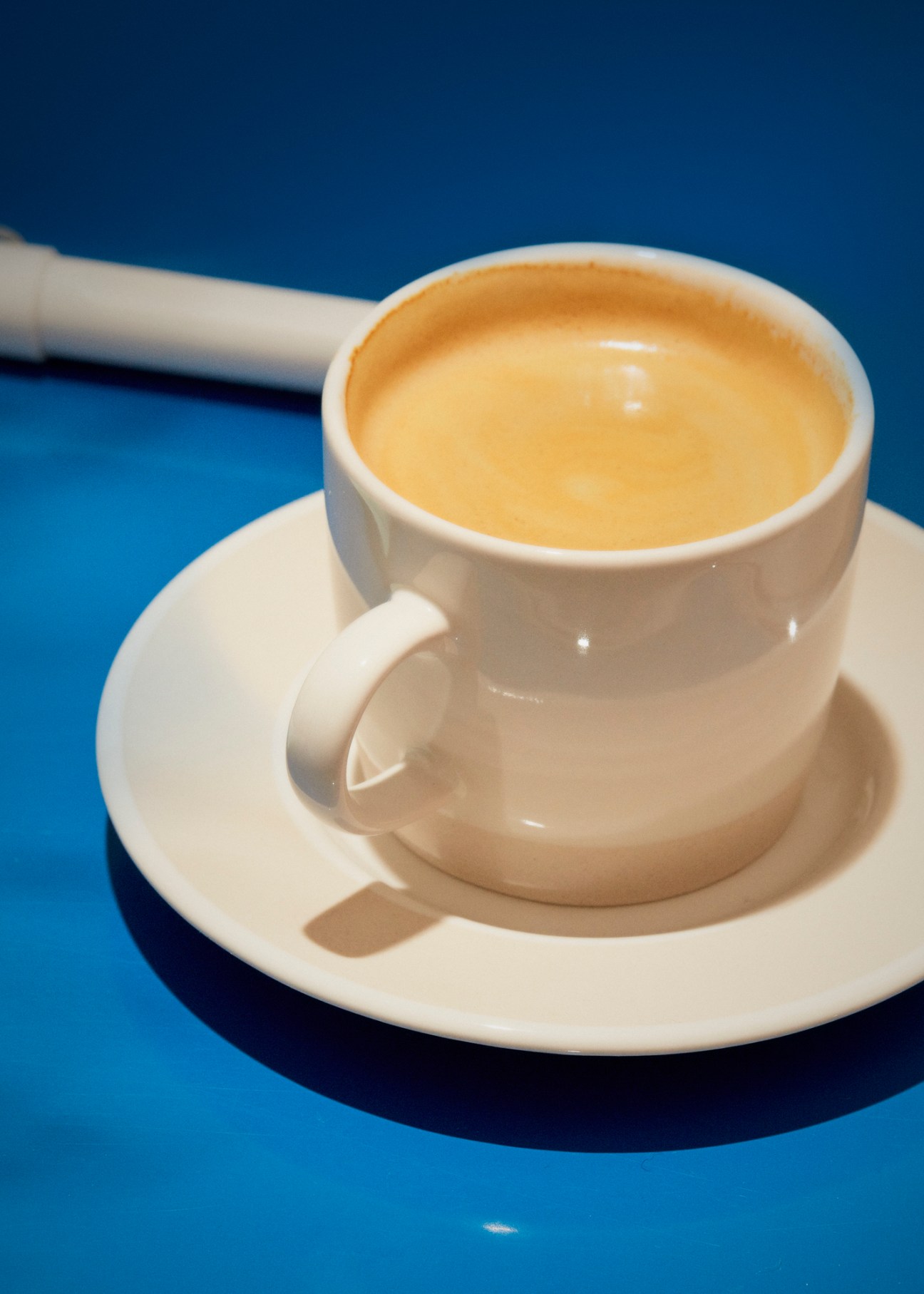 White coffee cup and saucer by David Mellor on blue surface