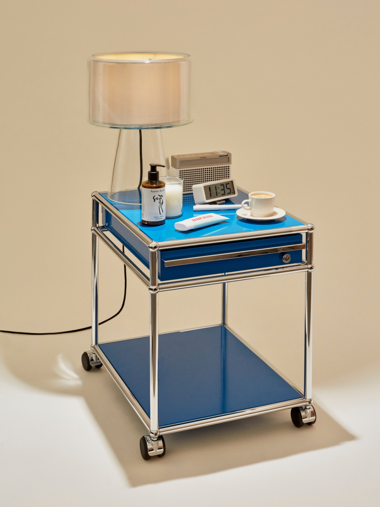 Modern blue bedside table with chrome frame, table lamp, clock, skincare products, and coffee cup