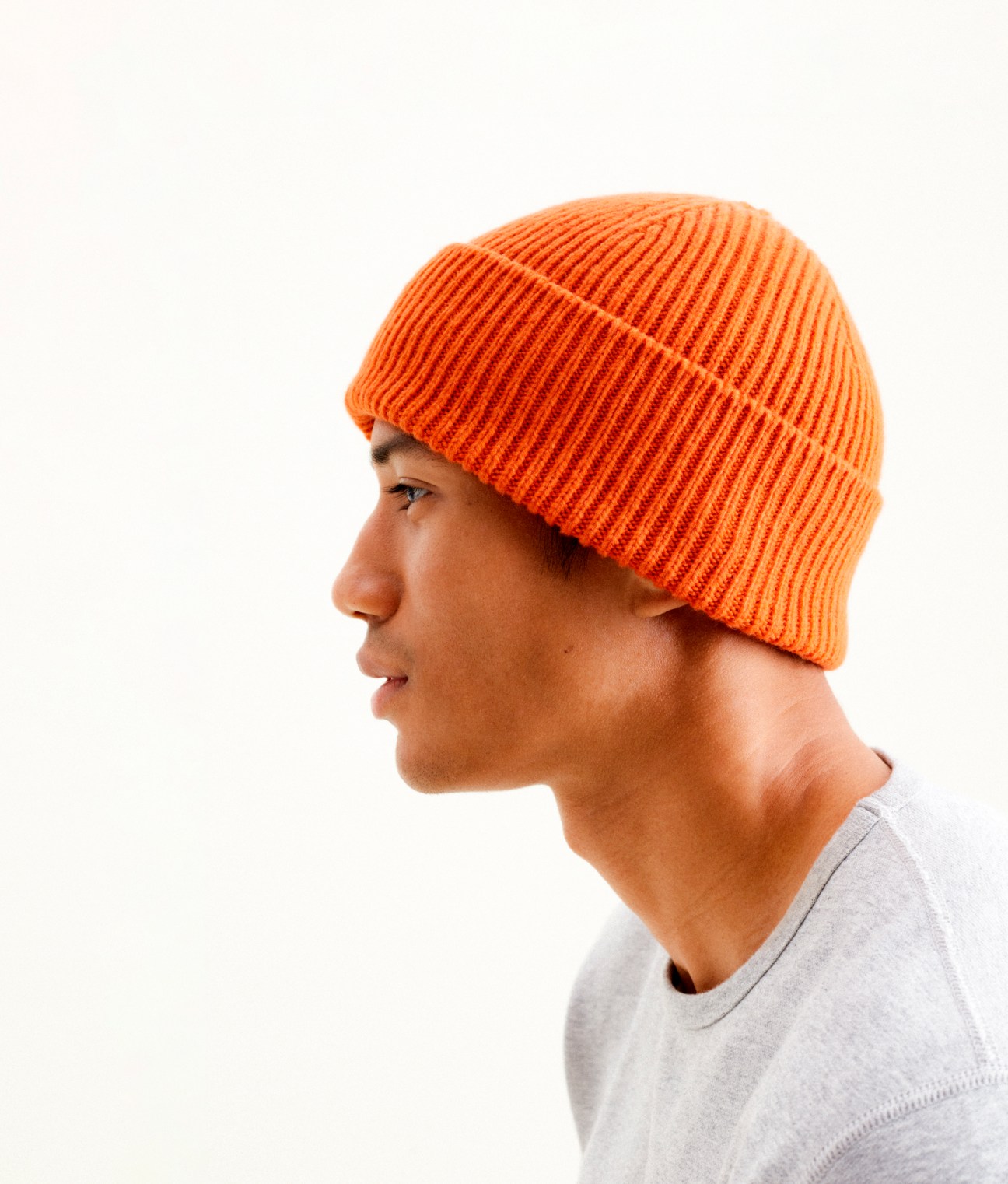 Man wearing an orange recycled cashmere beanie by Organic Basics x Monocle with a grey t-shirt.