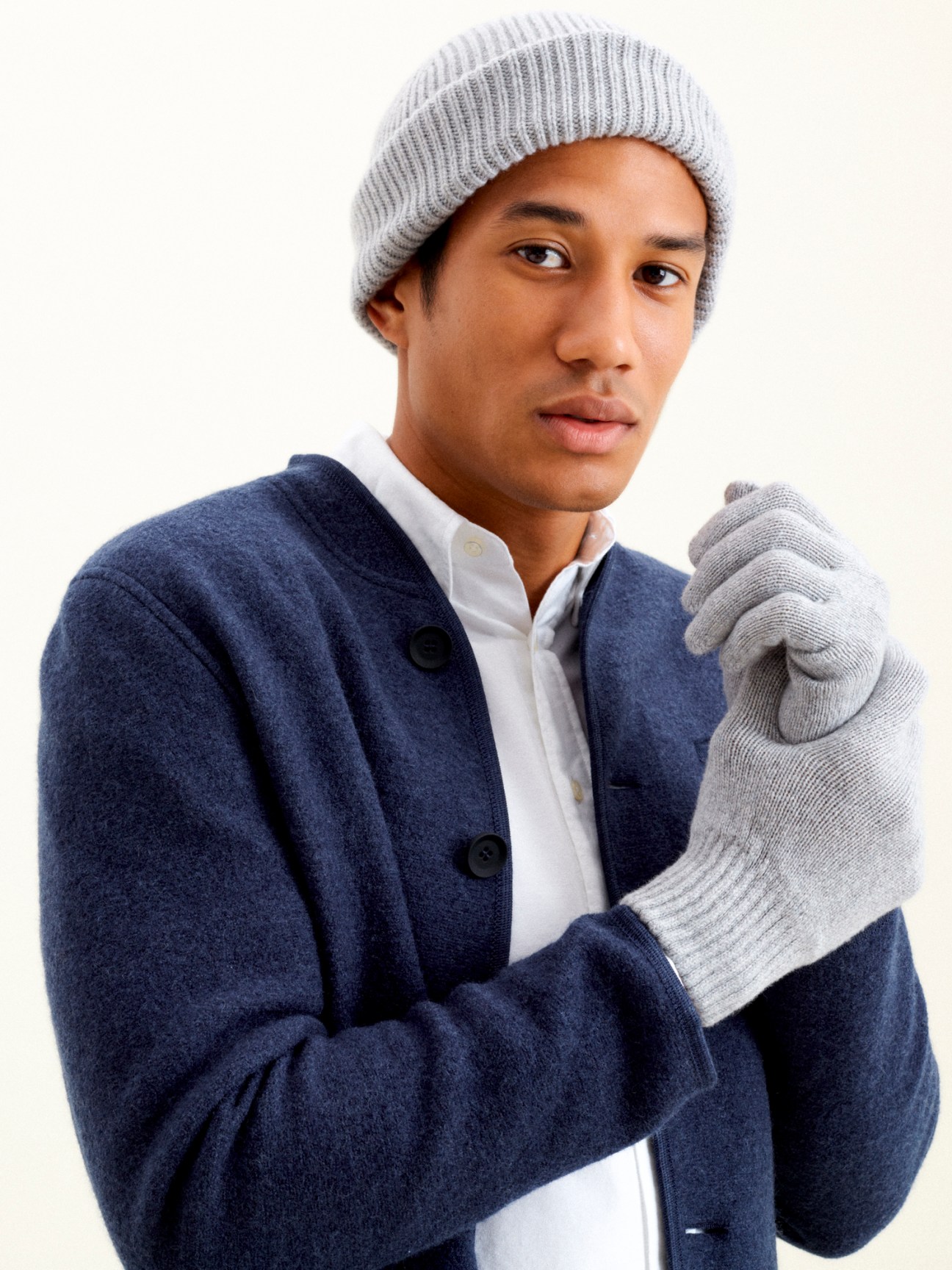 Person wearing light grey knitted beanie and matching gloves with navy cardigan over white shirt