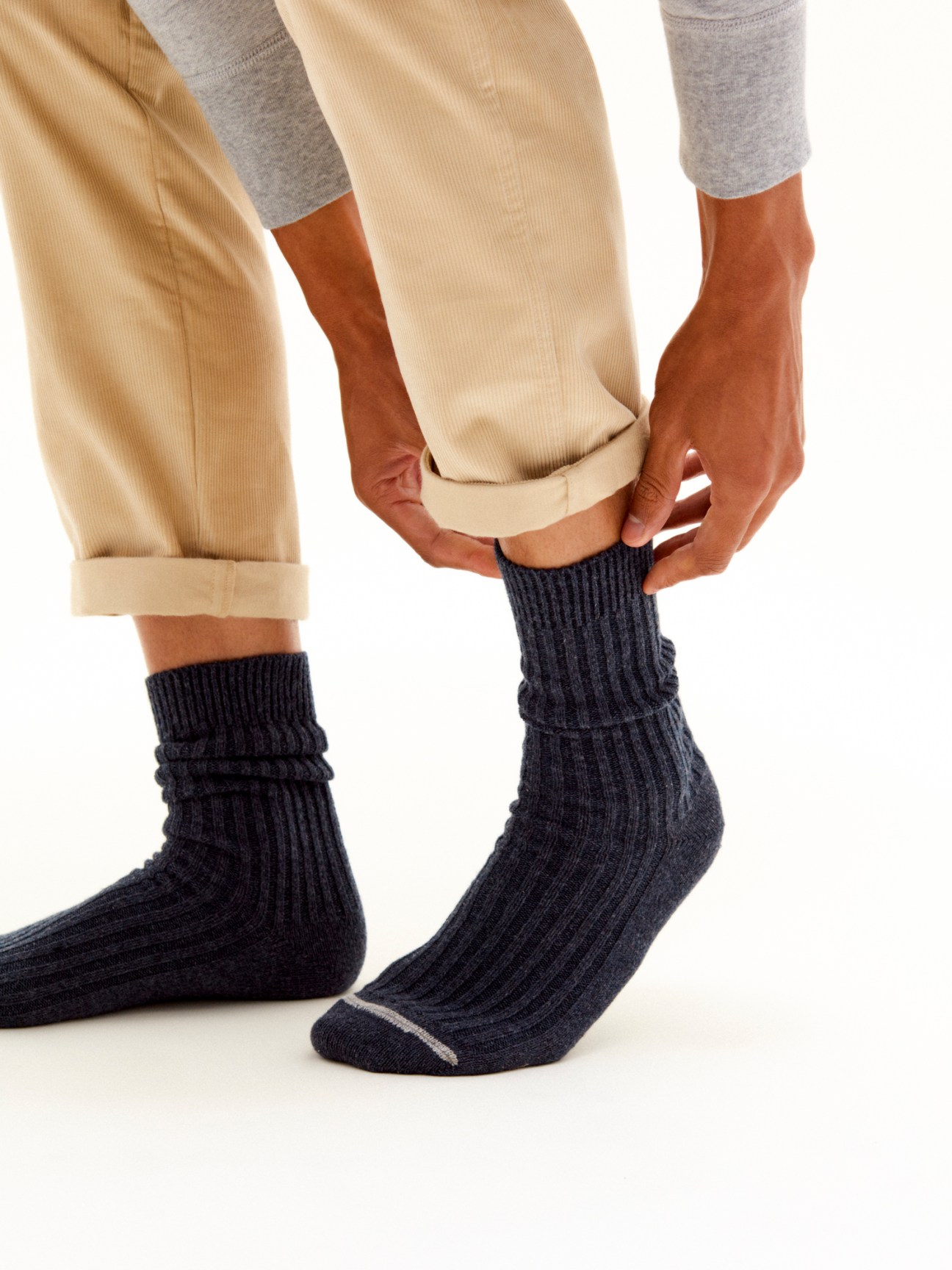 Person wearing navy melange ribbed wool Monocle socks adjusting beige corduroy trouser cuffs