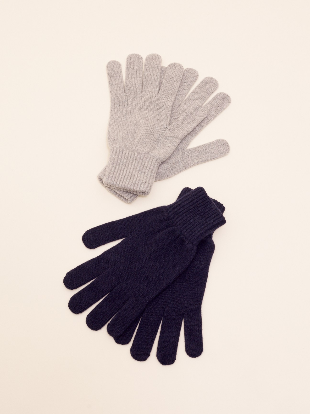 Two pairs of knitted gloves in light grey and dark navy blue displayed on neutral background