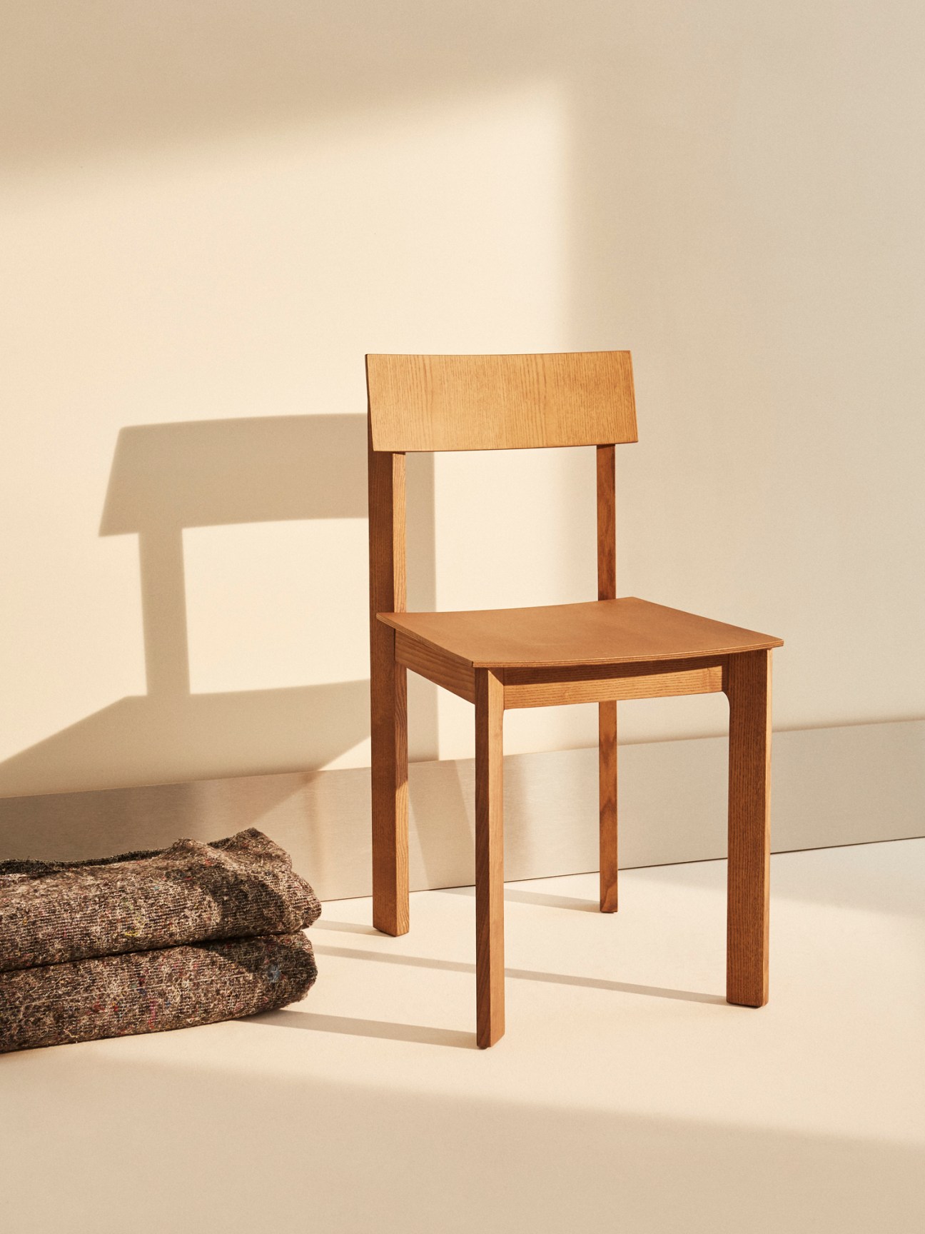 Candid dining chair in stained ash with distinctive angled legs that converge toward the center of the seat