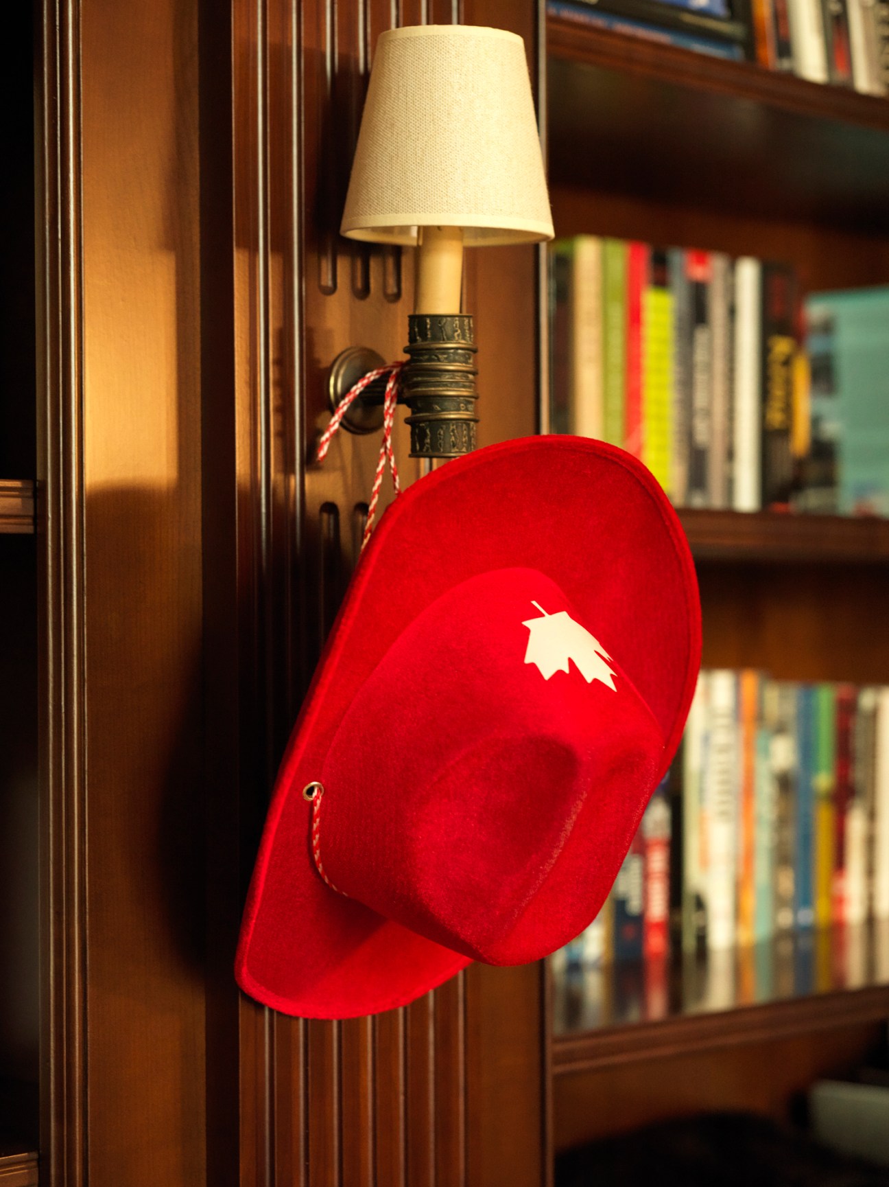 Red hat with white maple leaf hanging on wooden bookshelf in library