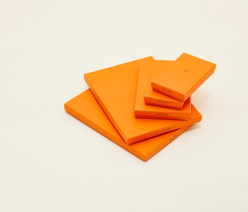 Orange leather accessories and packaging from Treuleben x Monocle collaboration displayed on neutral background