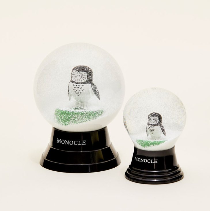 Two glass snow globes with Monochan owl character inside on black bases labeled MONOCLE