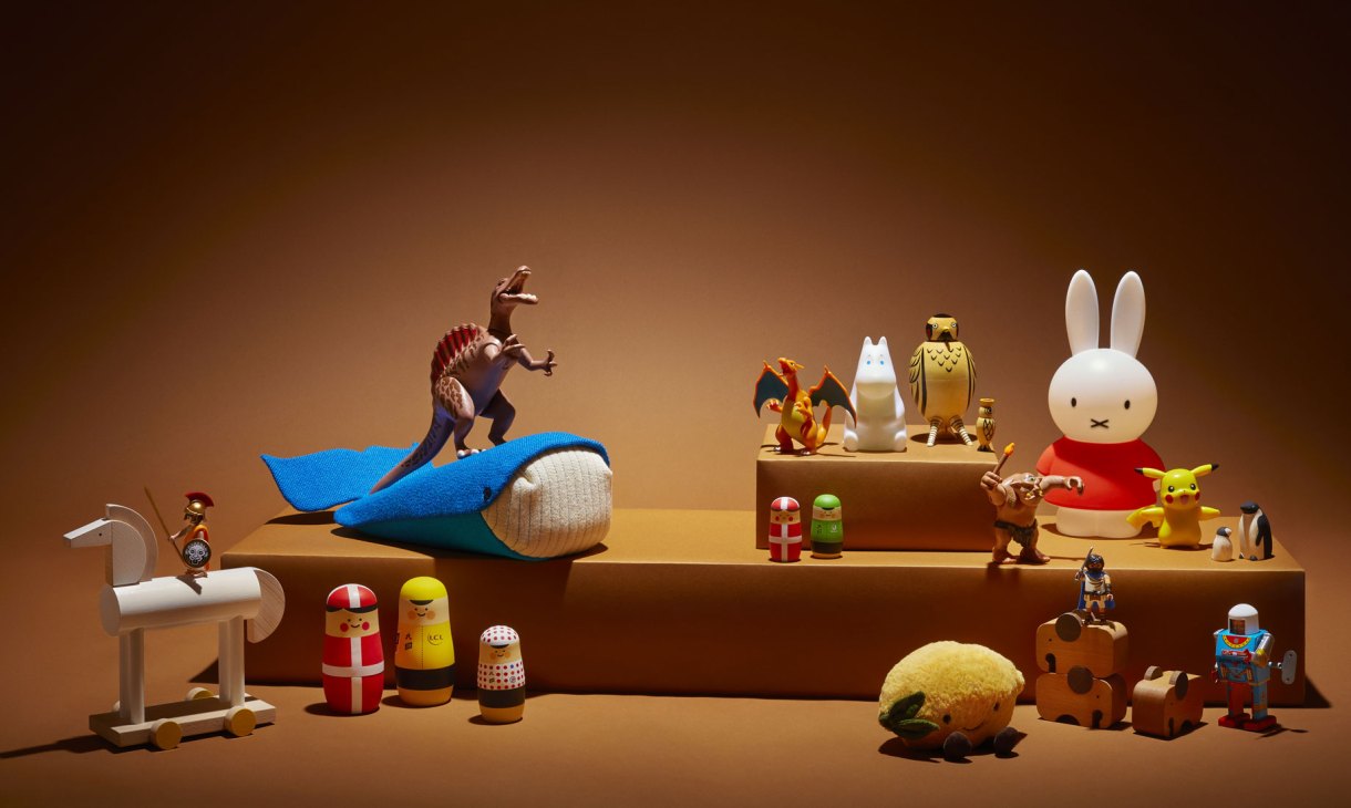 Assorted children's toys and decorative objects arranged on wooden stepped display against warm brown background