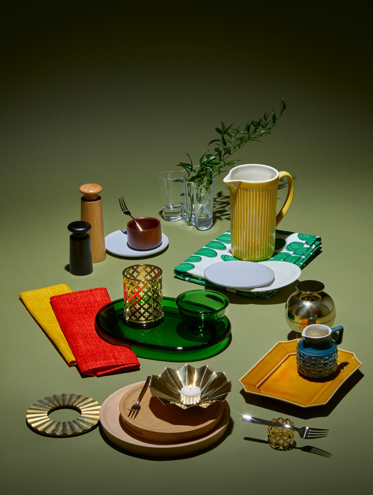 Stylish tableware and serving pieces arranged on green surface including plates, jugs, napkins, and utensils