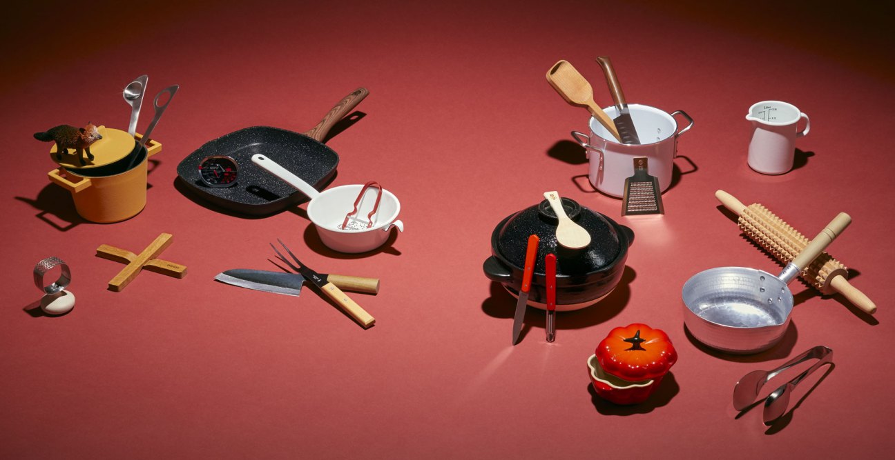 Various kitchen utensils and cookware arranged on red background including pans, knives, spoons and measuring tools