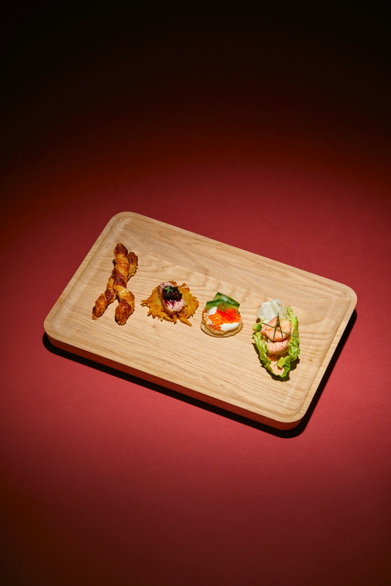Four elegant appetizers arranged on a wooden serving board against a burgundy gradient background