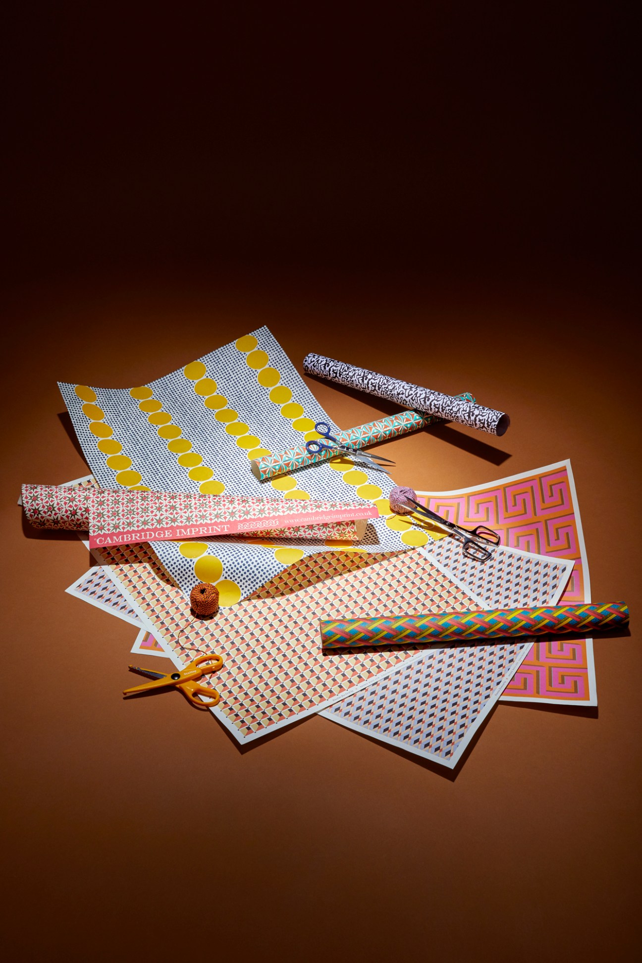 Assorted colorful gift wrapping papers, ribbons, and scissors arranged on warm brown surface for party supplies