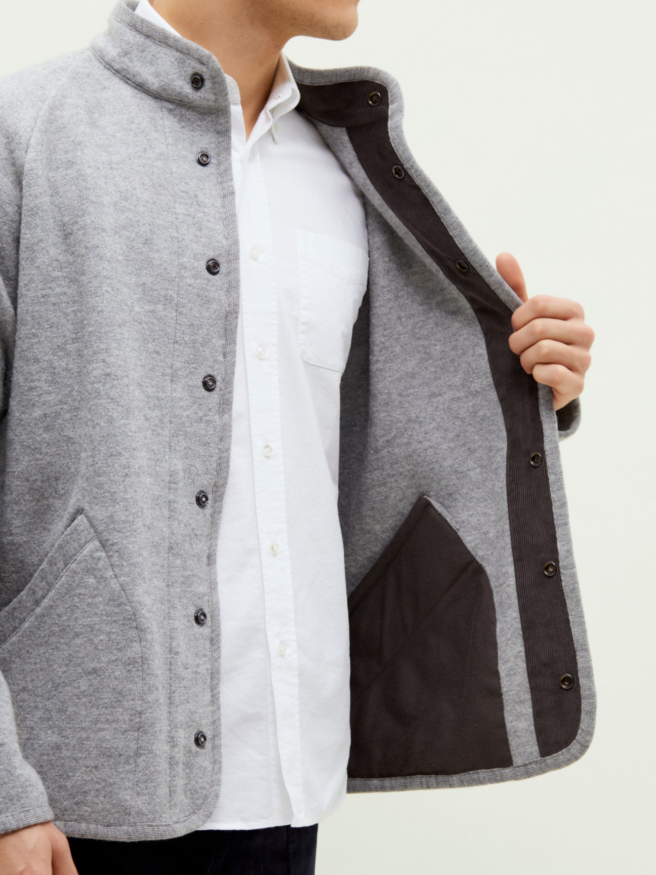 Model wearing Arpenteur x Monocle gray wool jacket with stand collar over white shirt, showing interior black lining.