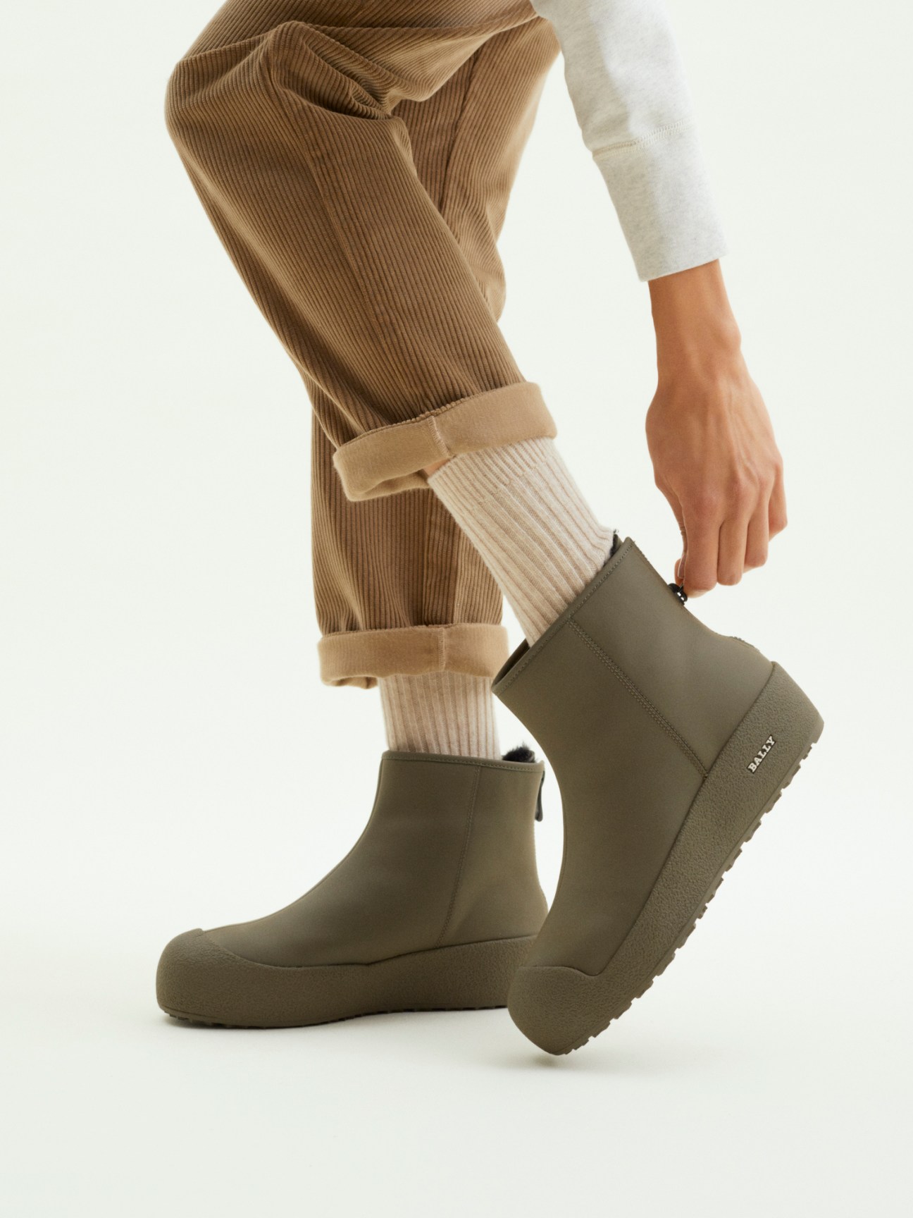Model wearing Bally x Monocle curling boot in olive green with cream socks and camel corduroy trousers.